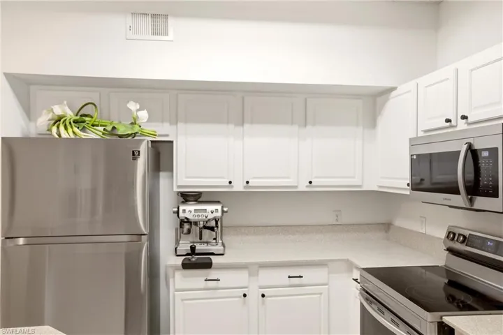 Kitchen with stainless steel appliances, white cabinetry, and light stone countertops