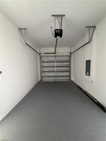 Single-car garage featuring a gray epoxy-coated floor, automatic garage door opener, and a wall-mounted electrical panel