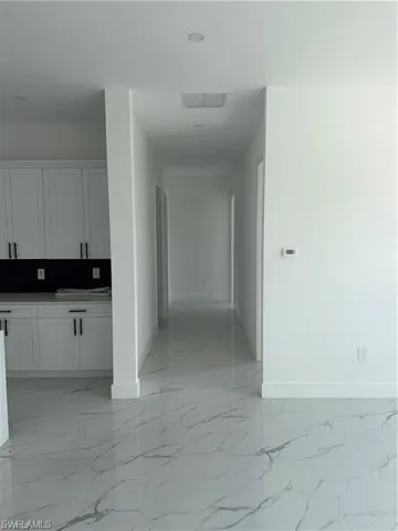 Spacious interior featuring pristine white walls, large format tile flooring with a subtle marble-like pattern, recessed lighting, and white cabinetry with black hardware