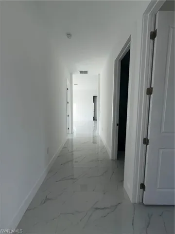 Hallway featuring polished tile flooring with a marble-like pattern, white walls, and bright white trim