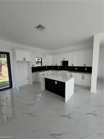 Kitchen featuring white cabinetry with dark hardware, dark countertops, a large center island with a white waterfall edge countertop, and large format white tile flooring with grey veining