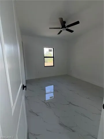 Spacious room featuring large format tile flooring with a marble-effect pattern, a contemporary ceiling fan, and a single window