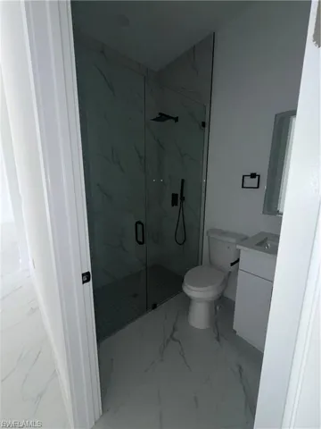 Modern bathroom featuring a glass-enclosed shower with black fixtures, a white vanity with integrated sink, and white-patterned tile flooring