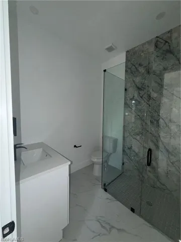 Bathroom featuring a glass-enclosed shower with marble-look tile, a white vanity with an integrated sink, and large format marble-look floor tile