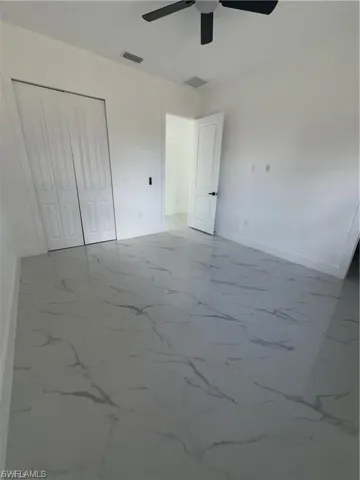 Spacious interior room featuring large format tile flooring with a marble-effect pattern, white walls, and a ceiling fan
