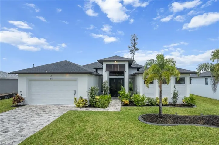 Prairie-style home featuring decorative driveway, a garage, a front yard, a shingled roof, and stucco siding