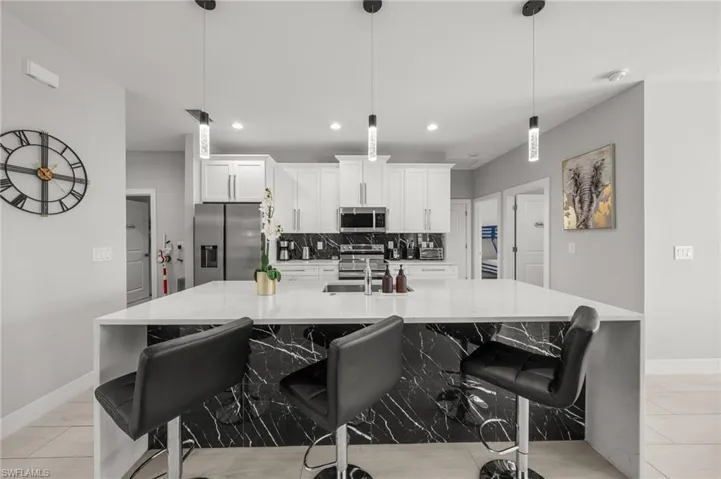 Kitchen featuring stainless steel appliances, decorative backsplash, a large island with sink, white cabinets, and recessed lighting