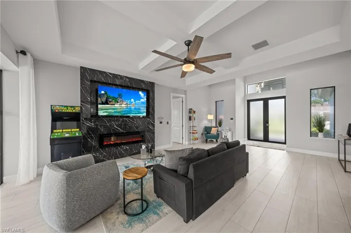 Living room featuring a high end fireplace, a ceiling fan, french doors, coffered ceiling, and a raised ceiling
