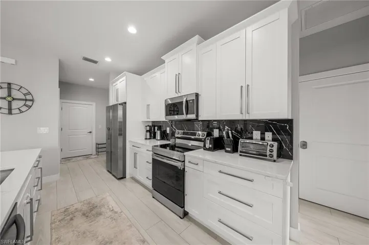 Kitchen with stainless steel appliances, light countertops, white cabinetry, recessed lighting, and backsplash