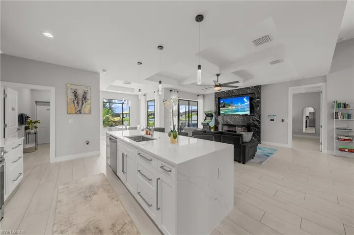 Kitchen featuring ceiling fan, white cabinetry, hanging light fixtures, a kitchen island with sink, and light stone countertops