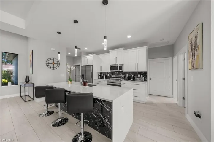Kitchen with stainless steel appliances, a large island with sink, white cabinets, a breakfast bar, and decorative backsplash