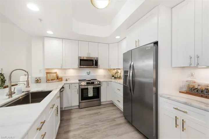 Kitchen with stainless steel appliances, white cabinets, recessed lighting, and light stone counters