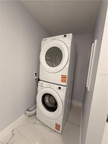 Laundry area featuring marble look tiles and stacked washing machine and dryer
