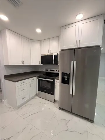 Kitchen featuring stainless steel appliances, white cabinetry, light marble finish flooring, recessed lighting, and dark countertops