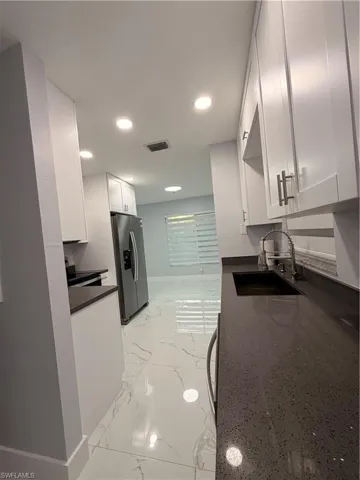 Kitchen View with white cabinets, light marble finish floors, fridge, dark stone countertops, and range