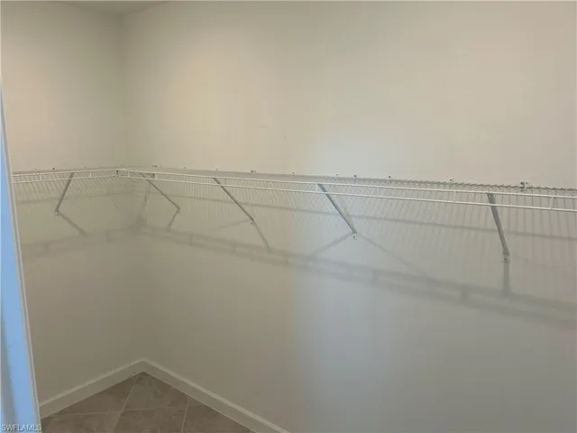 Corner closet featuring white wire shelving, light neutral wall paint, and tiled flooring with coordinating baseboards