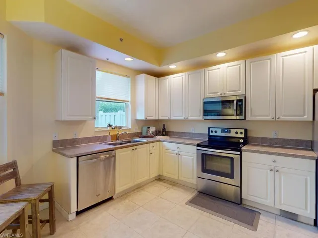 Kitchen with sink, light tile floors, white cabinetry, and appliances with stainless steel finishes