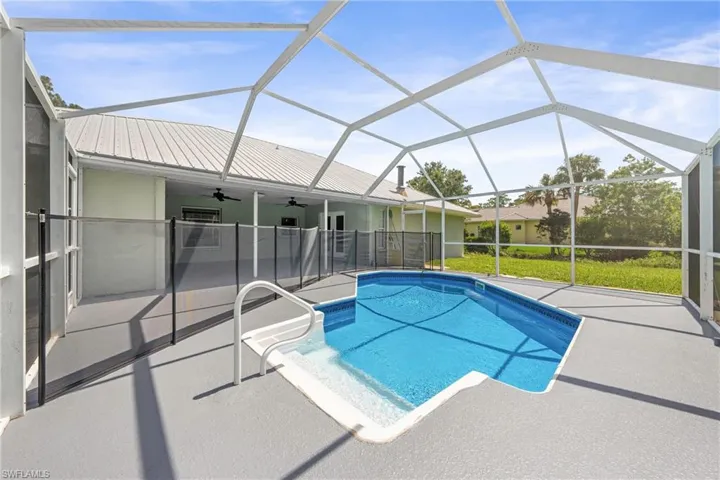 Screened pool enclosure featuring an in-ground swimming pool with integrated steps, a metal pool safety fence, and a spacious concrete deck