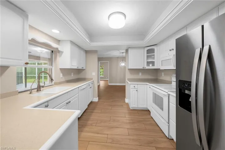Galley kitchen featuring white cabinetry, light-toned countertops, stainless steel appliances, wood-finish flooring, and a window overlooking a screened patio