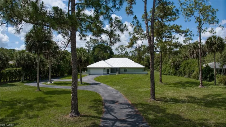 Ranch-style residence featuring a white roof and light green siding, situated on a substantial grassy lot with mature pine and palm trees