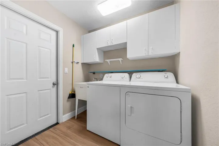 Dedicated laundry space featuring a utility sink, wood-finish flooring, and white upper cabinetry