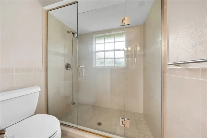 Glass-enclosed shower featuring a tiled surround and floor, chrome fixtures, and a window