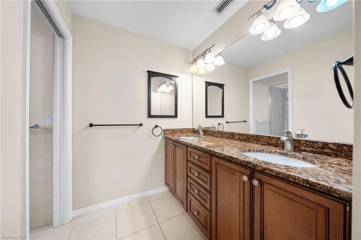 Dual vanity with granite countertops, integrated sinks, wood-finish cabinetry, and brushed nickel fixtures