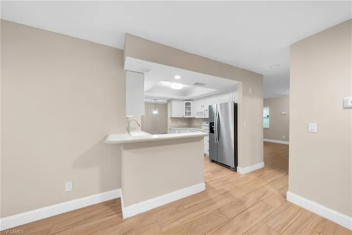 Kitchen pass-through with a breakfast bar, stainless steel refrigerator, light wood-finish flooring, white cabinetry, and recessed lighting