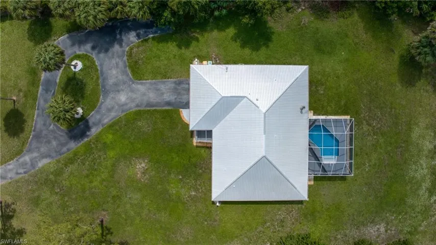 Aerial representation of the property featuring a light-colored hip roof, an attached screened pool enclosure, a paved circular driveway, and surrounding green landscaping