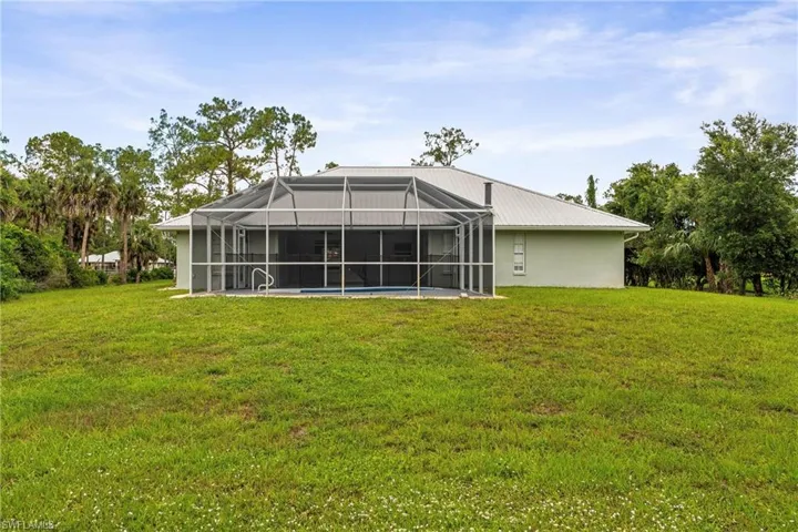 Expansive green lawn surrounds the residence, featuring a screened-in pool enclosure