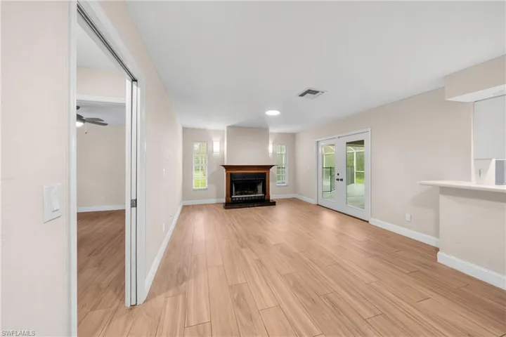Spacious room featuring wood-finish flooring, a traditional fireplace with a dark wood mantel, and double glass doors leading to an outdoor area