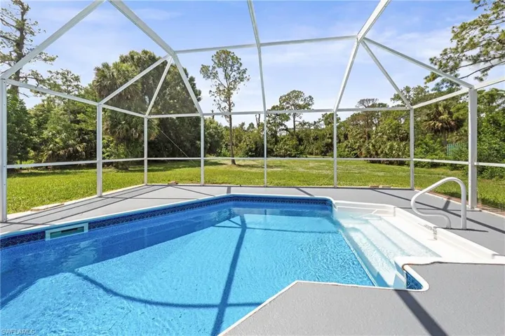 Screened outdoor pool with blue tile border, integrated steps, and a handrail, surrounded by a textured deck