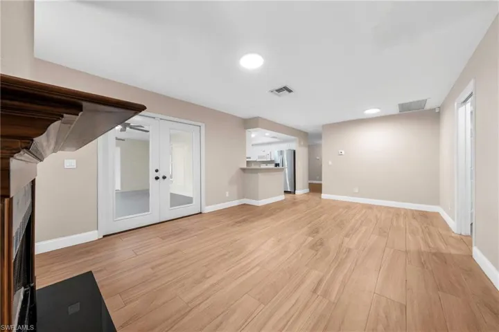 Spacious living area featuring wood-look flooring, recessed lighting, a decorative fireplace with a dark wood mantel, and double French doors with clear glass panels
