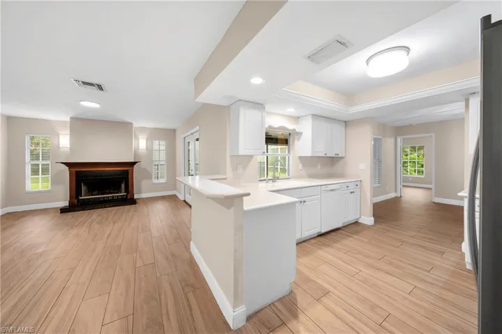 Open-concept living space with wood-finish flooring, a built-in fireplace featuring a dark wood mantel, and a kitchen island with a breakfast bar