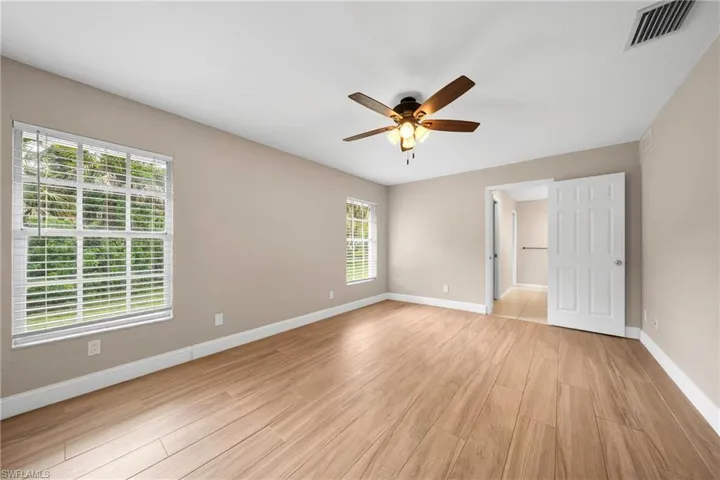 Spacious room featuring wood-finish flooring, neutral wall tones, two windows with blinds, and a ceiling fan with integrated lighting