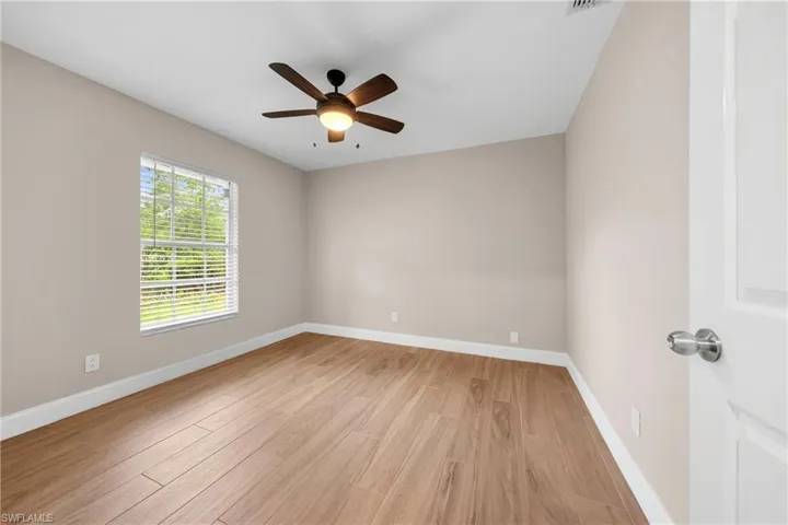 Room featuring wood-finish flooring, a ceiling fan with integrated lighting, a single window with blinds, and neutral wall paint