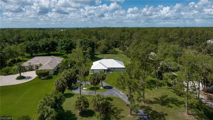 Expansive property featuring two residences, lush green lawns, mature trees, and paved driveways