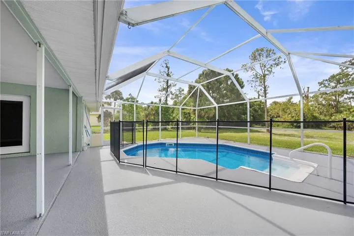 Screened-in pool area featuring a built-in spa, safety fencing, and an expansive covered patio with concrete flooring