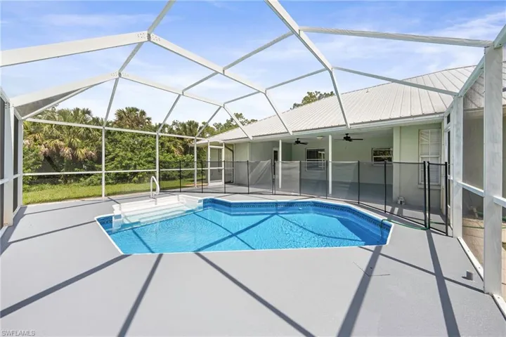 Screened outdoor pool area featuring an in-ground swimming pool with integrated steps, a surrounding safety fence, and a spacious patio area