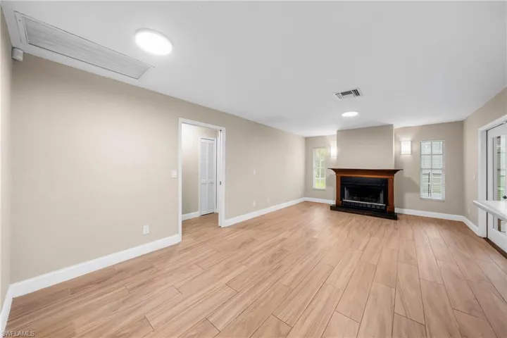 Spacious room featuring wood-finish flooring, a prominent fireplace with a wood mantle, multiple windows, and recessed lighting