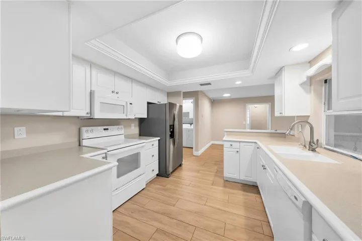 Kitchen featuring white cabinetry, light-toned countertops, wood-finish flooring, recessed lighting, and a tray ceiling with crown molding