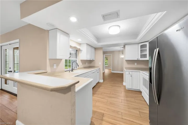 Kitchen featuring wood-look tile flooring, white cabinetry, light-toned countertops, a breakfast bar, and stainless steel appliances