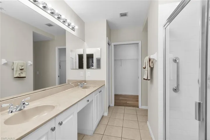 Full bath featuring double vanity, a stall shower, a spacious closet, and light tile patterned floors