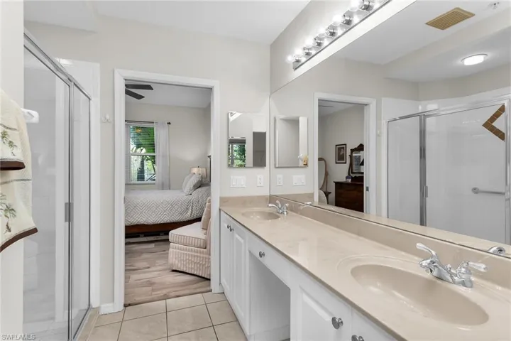 Ensuite bathroom with a shower stall, double vanity, light tile patterned floors, and ceiling fan