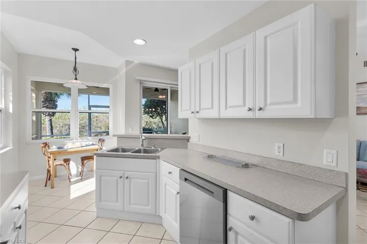 Kitchen featuring stainless steel dishwasher, white cabinets, decorative light fixtures, and a peninsula