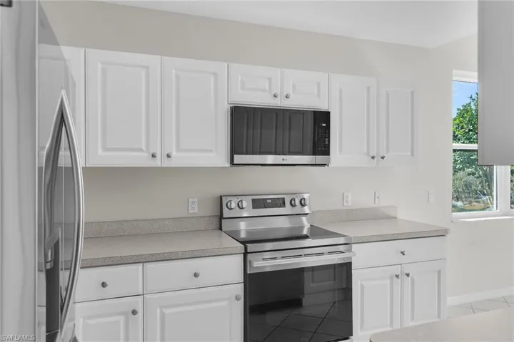 Kitchen with stainless steel appliances, white cabinets, light countertops, and light tile patterned flooring