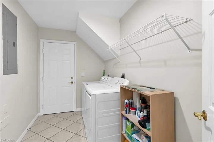 Laundry area with electric panel, light tile patterned floors, and washing machine and dryer