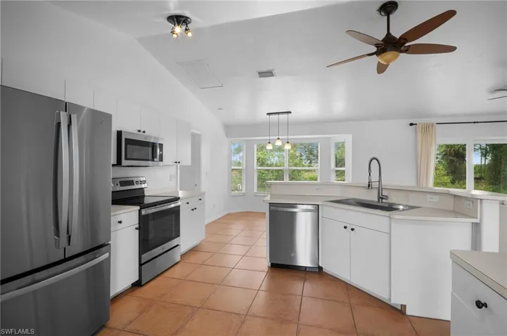 Kitchen with stainless steel appliances, white cabinets, light tile patterned flooring, light countertops, and vaulted ceiling