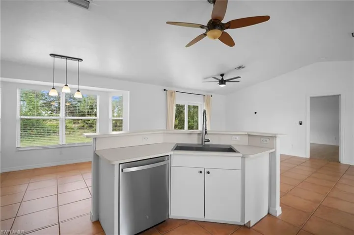 Kitchen with a kitchen island with sink, light tile patterned flooring, light countertops, stainless steel dishwasher, and vaulted ceiling