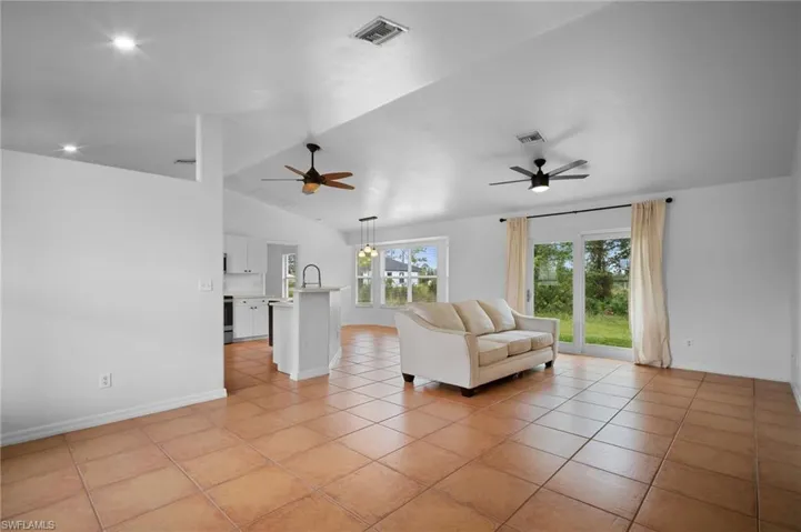 Living room with lofted ceiling, light tile patterned flooring, ceiling fan, and recessed lighting